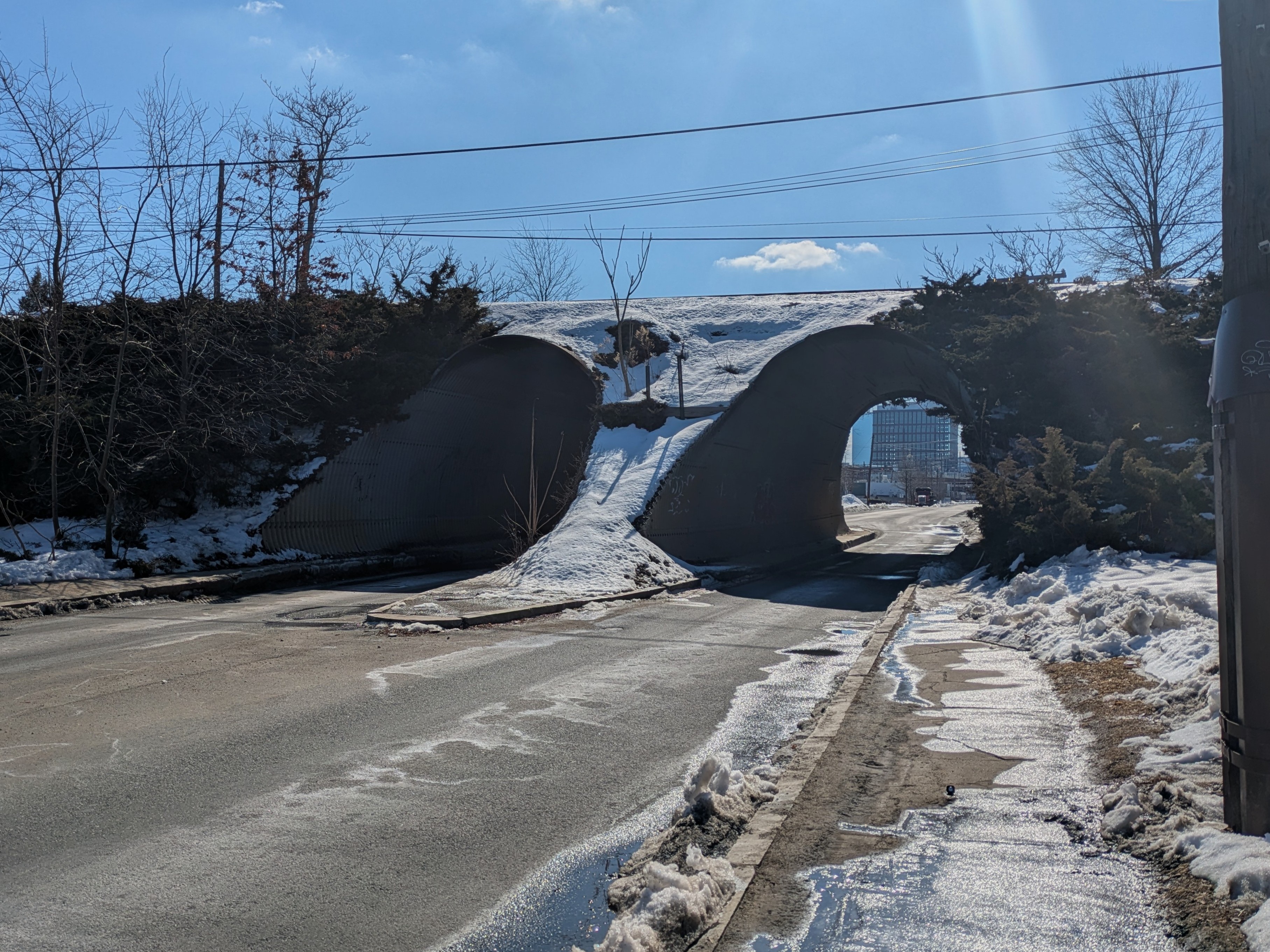Train tracks run across an elevated berm. Two culvert-like tunnels underneath it, made of corrugated metal, allow the passage of traffic.