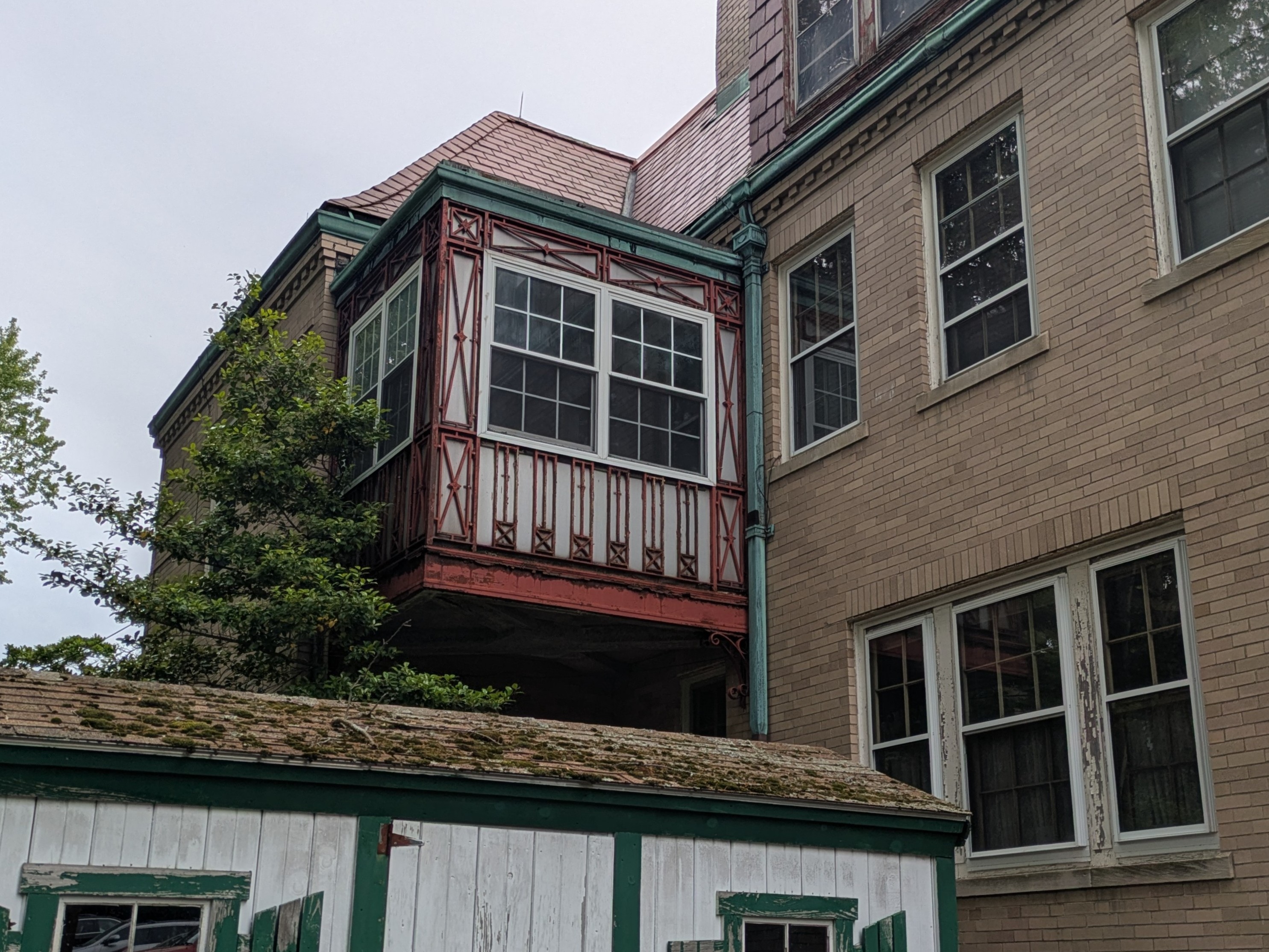 A tan brick building with a enclosed porch-like room hanging off it. The walls are decorated with elaborate red metalwork.