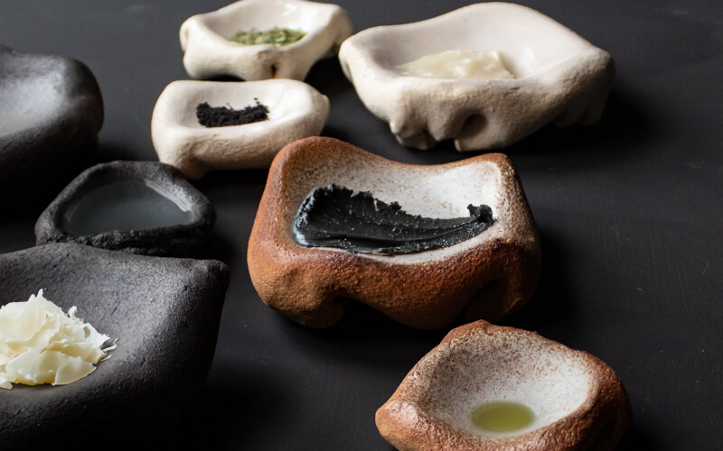 A scattering of small dishes made of stone, each containing ingredients like ash, olive oil, and wax.