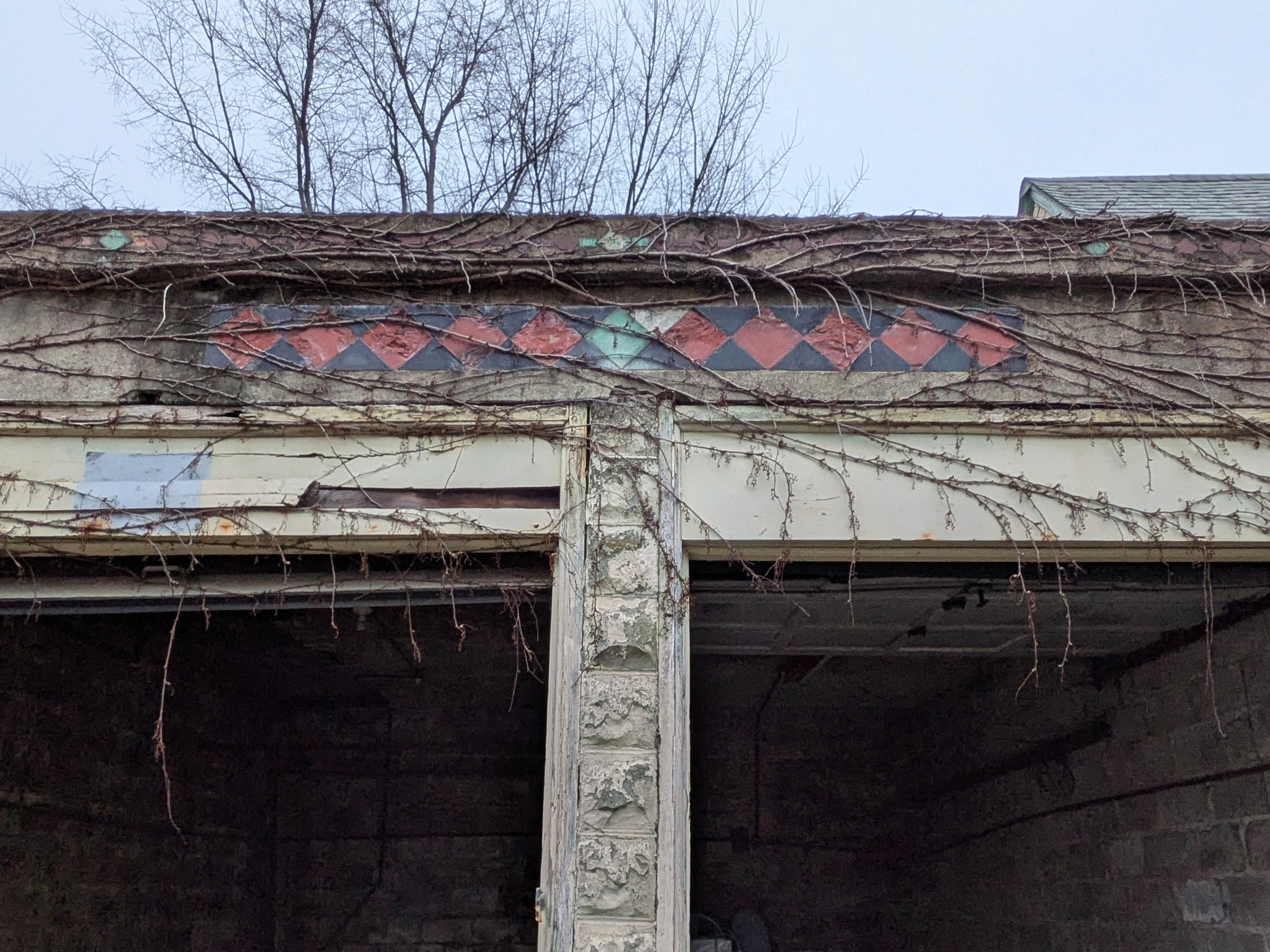 The cement lintel of a two-car garage. A strip of red-and-black checkerboard pattern is tiled along it. The centermost tile is mint green.